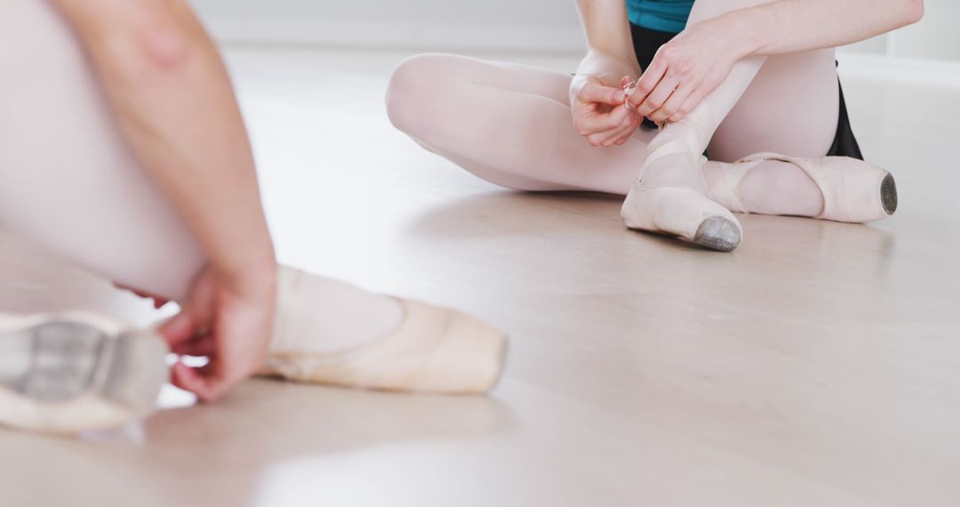 Two caucasian female ballet dancers sitting on floor tying pointe shoes at dance studio - Free Images, Stock Photos and Pictures on Pikwizard.com