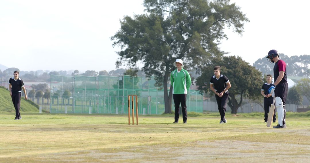 Cricket Players Practicing Bowling and Batting on Grassy Field
