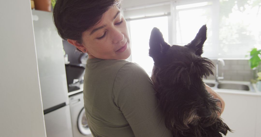 Caucasian woman holding her dog in the kitchen at home - Free Images, Stock Photos and Pictures on Pikwizard.com