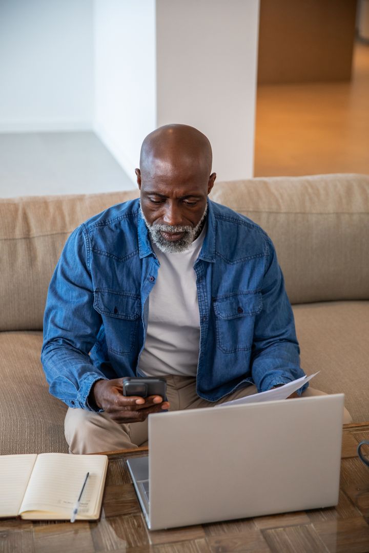 Senior Man Seeking Knowledge with Laptop, Smartphone, and Paperwork