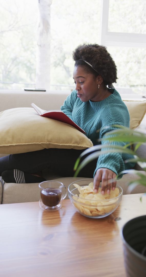 Woman Reading Book While Snacking on Chips and Tea at Home - Free Images, Stock Photos and Pictures on Pikwizard.com