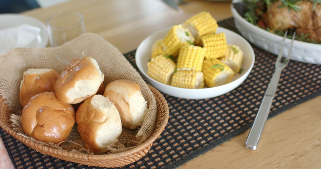 Wicker basket holding soft dinner rolls with buttered corn on rustic wooden table