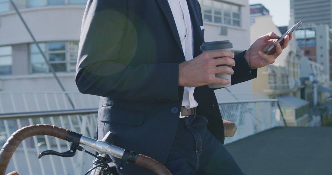 Businessman Holding Coffee Using Smartphone Bike on City Bridge - Free Images, Stock Photos and Pictures on Pikwizard.com