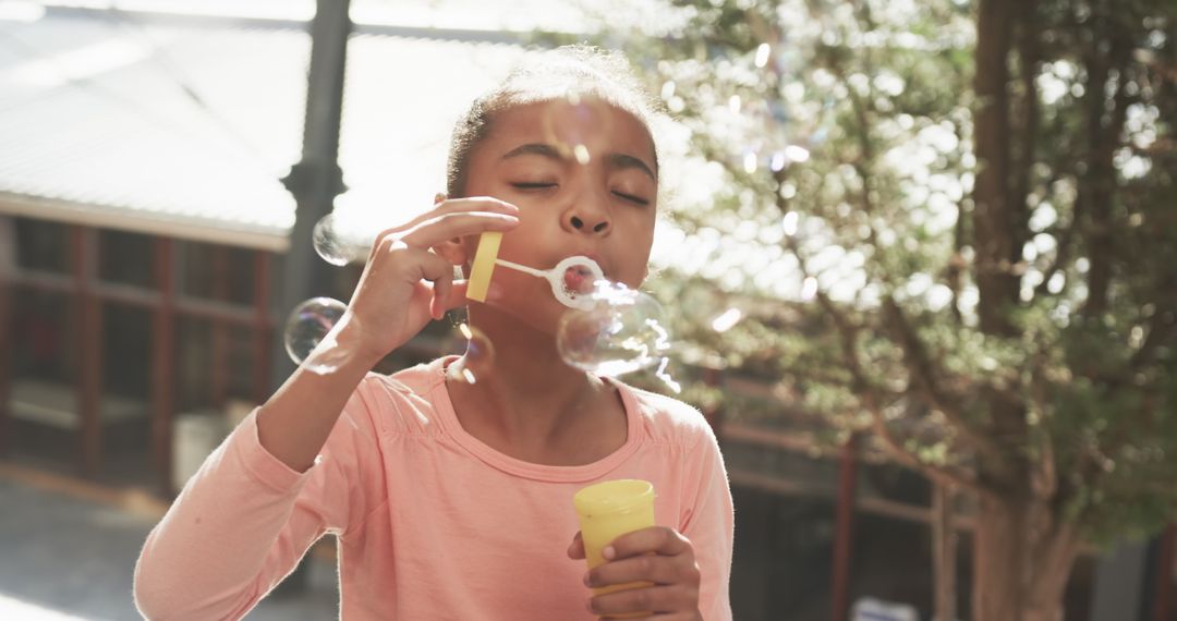 Young Girl Blows Bubbles Outdoors in Sunlit Yard