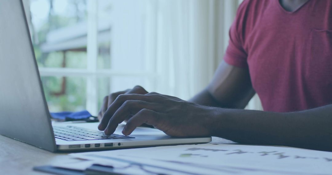 Focused Man in Red T-Shirt Working on Silver Laptop Near Window