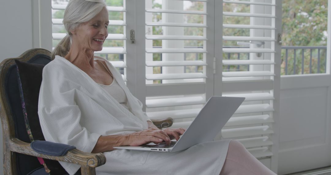 Older woman with laptop working from home in comfortable chair - Free Images, Stock Photos and Pictures on Pikwizard.com