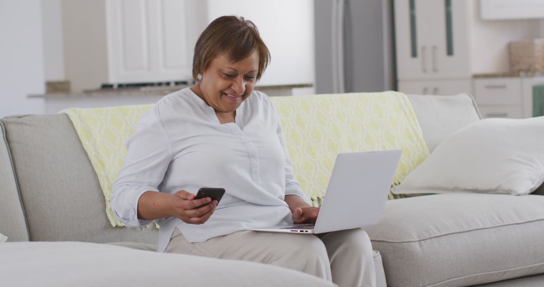 Mature Woman Smiling While Using Mobile Phone and Laptop at Home - Free Images, Stock Photos and Pictures on Pikwizard.com