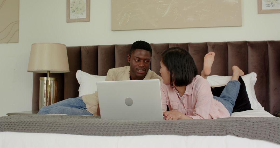 Multicultural Couple Planning Honeymoon with Laptop on Bed