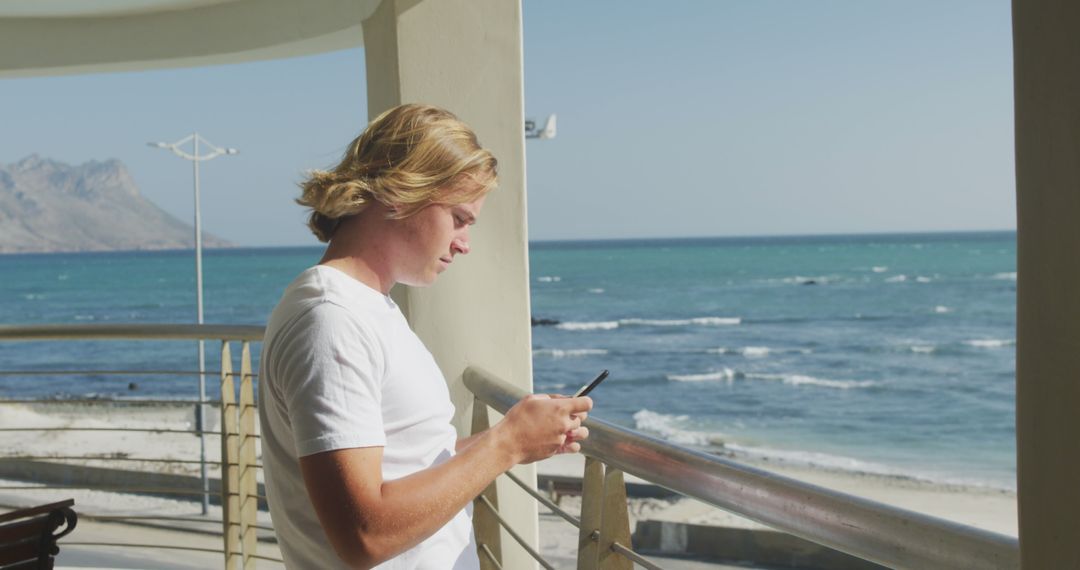 Young Man Using Smartphone on Oceanfront Balcony - Free Images, Stock Photos and Pictures on Pikwizard.com