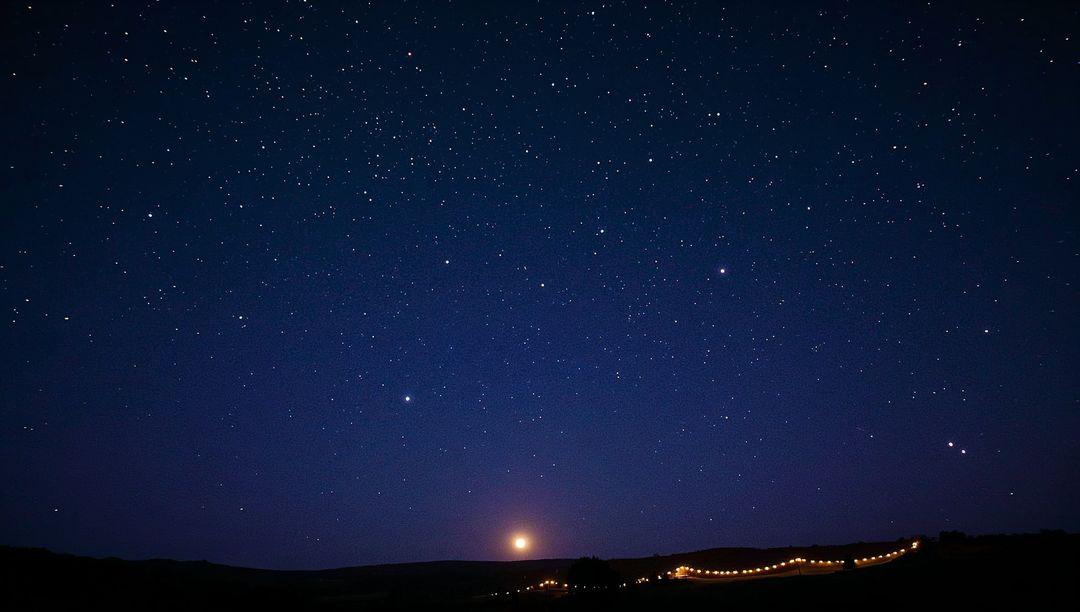 Glowing moonrise and starry sky stretching over rural rolling hills with warm lights