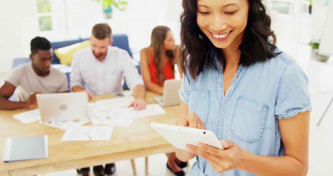 Smiling Woman Using Tablet with Colleagues Working in Background - Free Images, Stock Photos and Pictures on Pikwizard.com