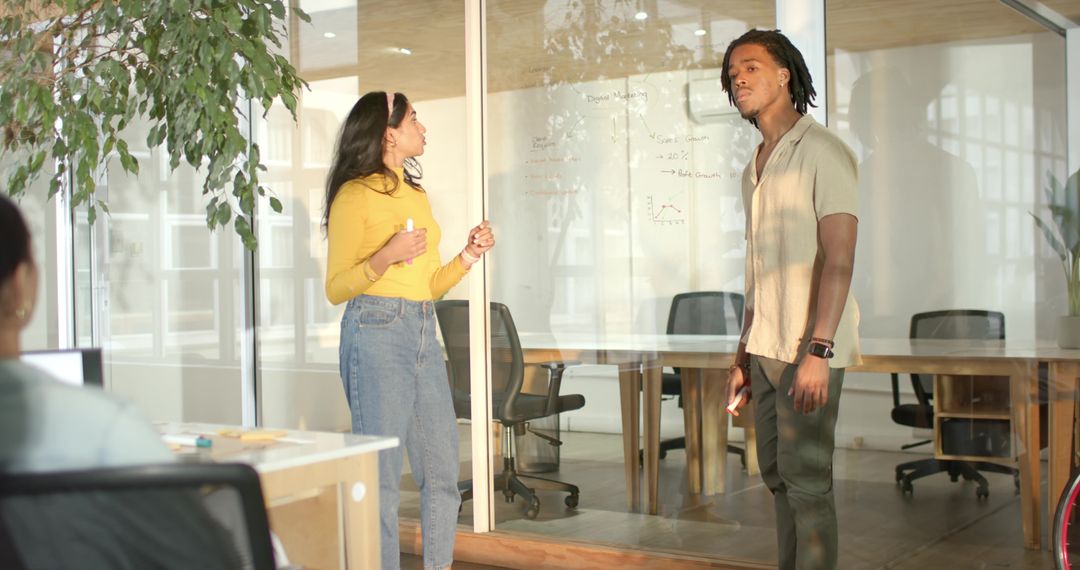 Diverse coworkers collaborating and brainstorming at glass-walled meeting space with marker