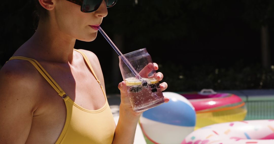 Woman Enjoying Refreshing Drink by Pool with Inflatables