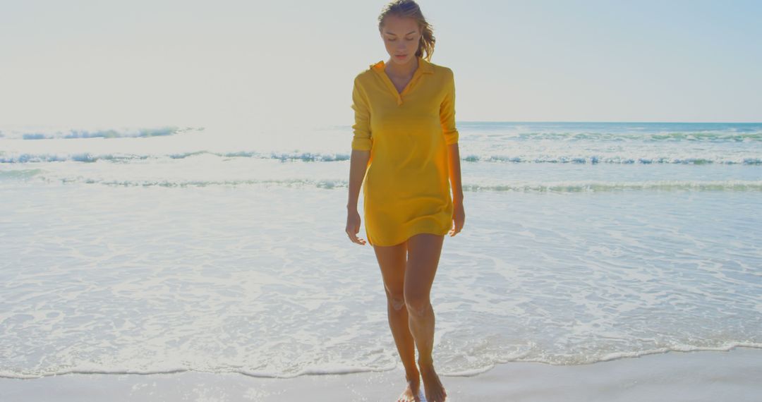 Woman Wearing Yellow Dress Walking on Beach Shoreline on Sunny Day - Free Images, Stock Photos and Pictures on Pikwizard.com