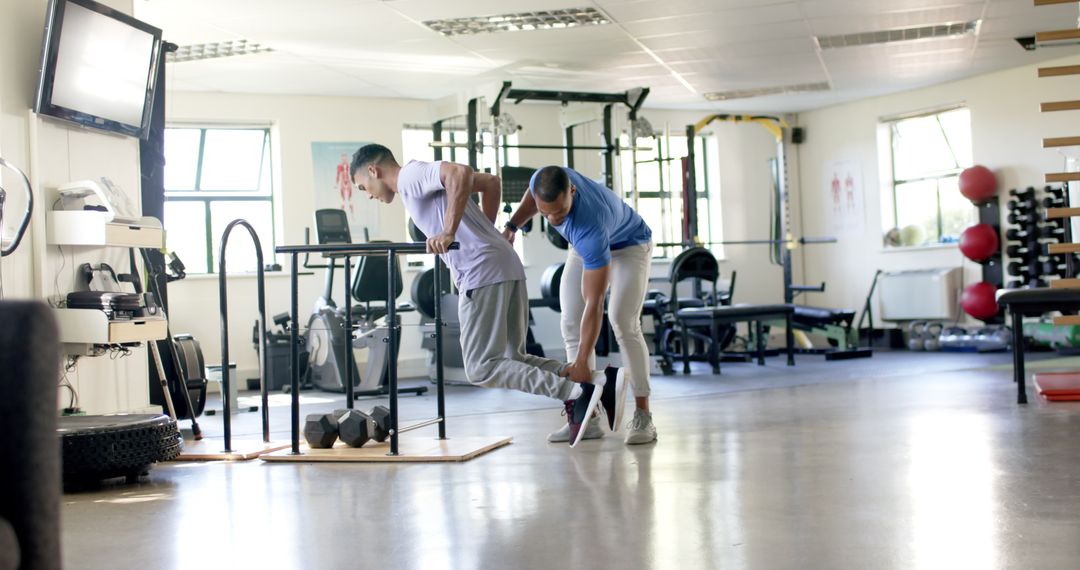 Trainer Assisting Disabled Man with Parallel Bar Exercise in Therapy Center