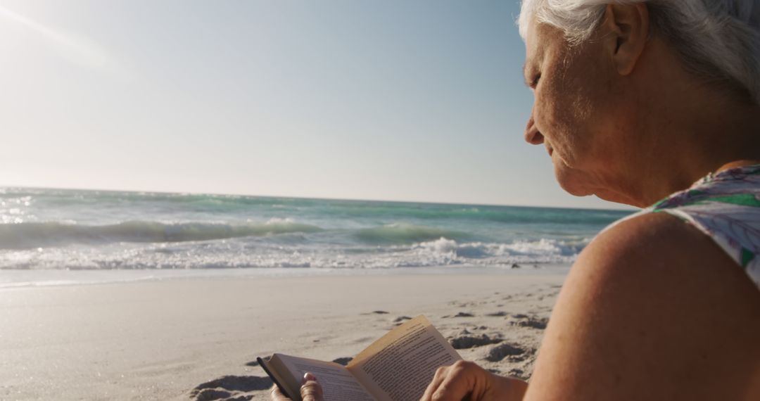 Senior Woman Reading Book on Sunny Beach - Free Images, Stock Photos and Pictures on Pikwizard.com