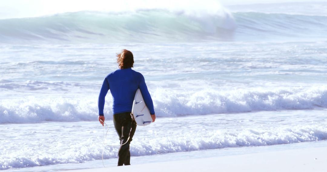 Surfer with blue wetsuit walking towards ocean waves - Free Images, Stock Photos and Pictures on Pikwizard.com