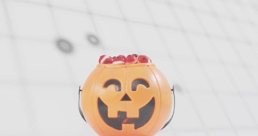 Happy Jack-o'-Lantern Candy Bucket Spilling Red Candies on Bright White Grid