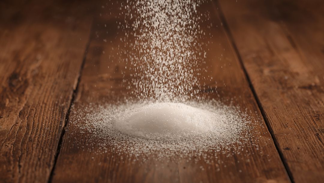White Granular Powder Falling on Rustic Wooden Table