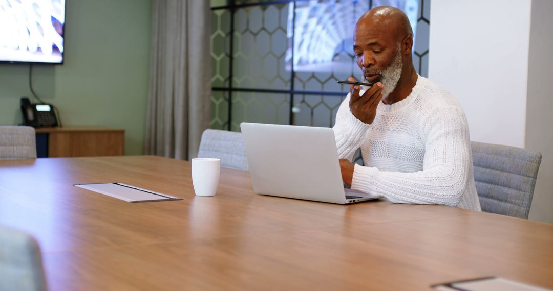 Businessman in modern office using laptop and speaking on smartphone - Free Images, Stock Photos and Pictures on Pikwizard.com