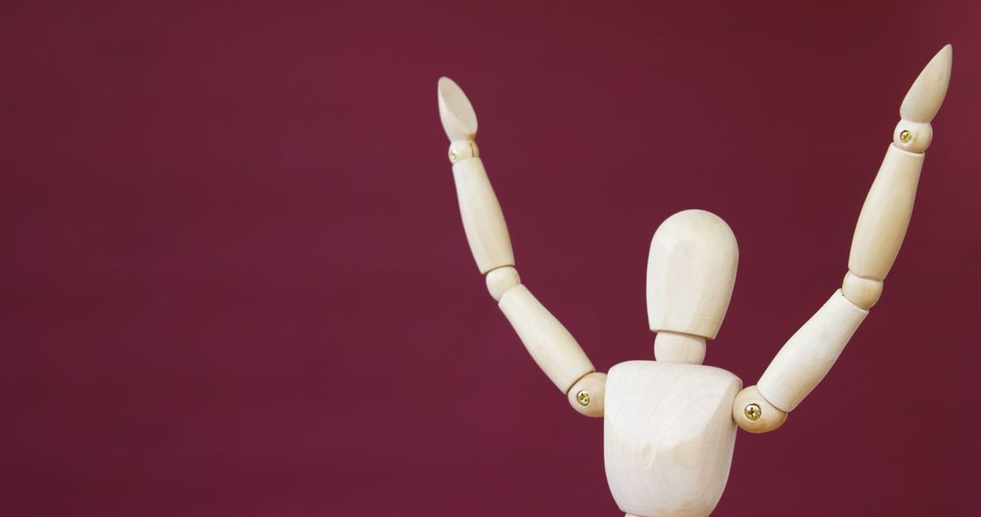A wooden artist's mannequin is posed with arms raised against a maroon background, with copy space - Free Images, Stock Photos and Pictures on Pikwizard.com