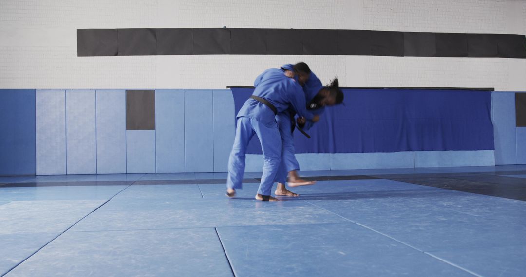 Martial Artists Practicing Throw Techniques in Gym with Blue Mat
