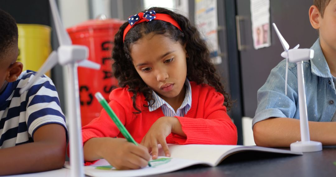Biracial Girl Writing with Wind Turbines in Classroom Focused on Renewable Energy