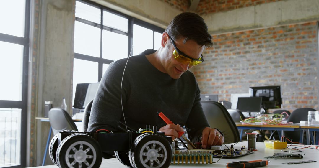 A young Caucasian man is focused on assembling or repairing a robotic vehicle, with copy space - Free Images, Stock Photos and Pictures on Pikwizard.com