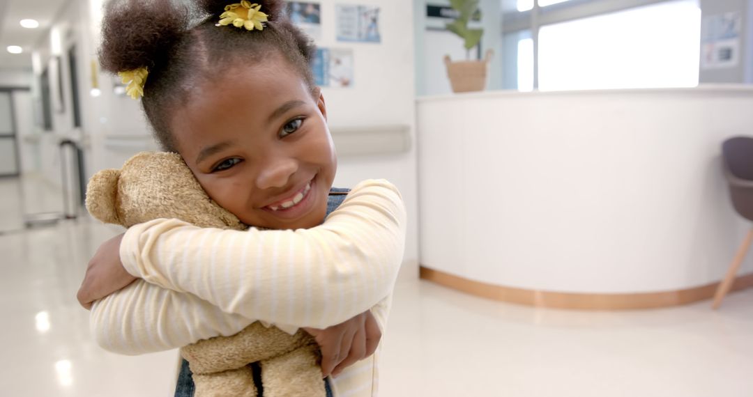 Happy African American Girl Hugging Teddy Bear in Hospital Lobby - Free Images, Stock Photos and Pictures on Pikwizard.com