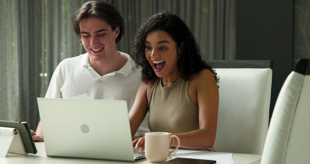 Happy Couple Laughing Together While Browsing Laptop at Home