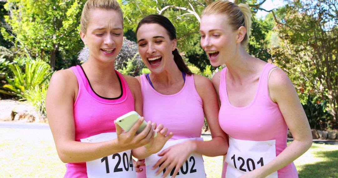 Female runners in pink sports tops laughing and checking phone during outdoor event - Free Images, Stock Photos and Pictures on Pikwizard.com