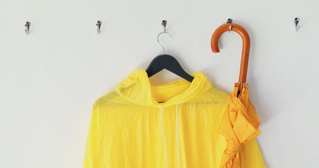 Yellow Raincoat and Umbrella on Hanger Against White Wall - Free Images, Stock Photos and Pictures on Pikwizard.com