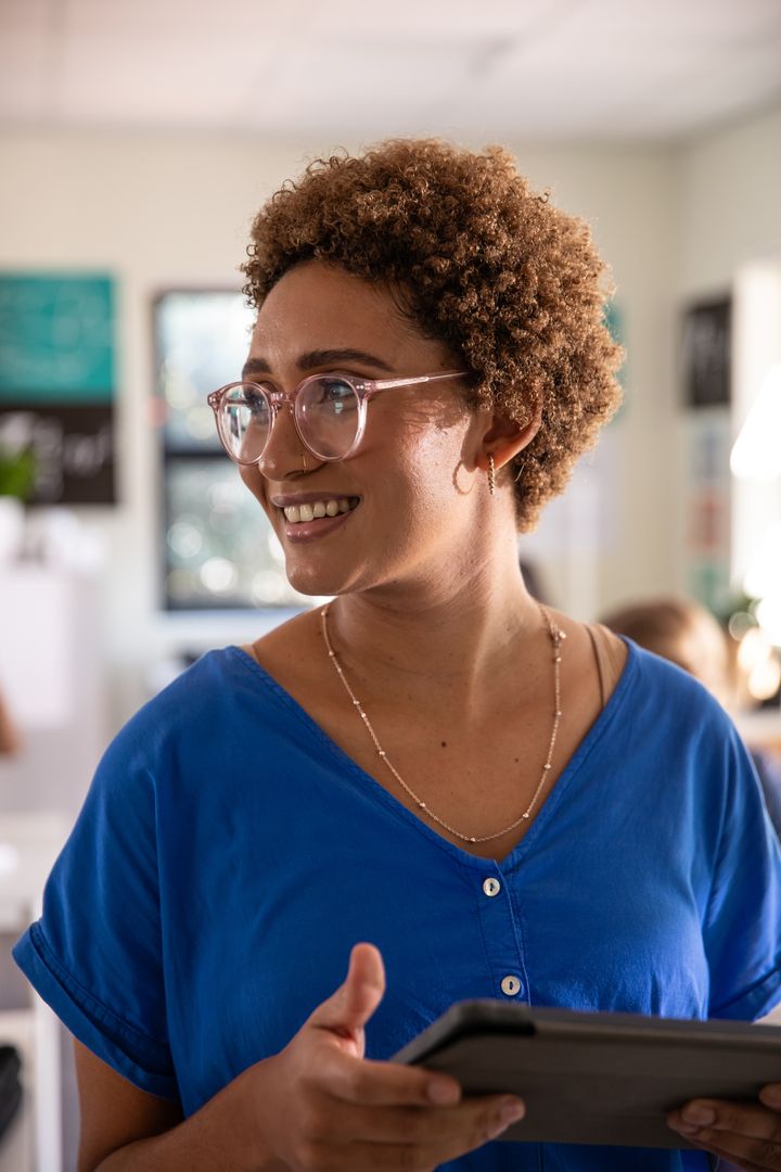 African American educator smiling and holding tablet while teaching in modern classroom