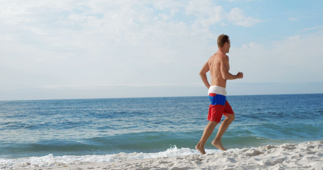 Man Running on Beach in Red and Blue Shorts on Sunny Day - Free Images, Stock Photos and Pictures on Pikwizard.com