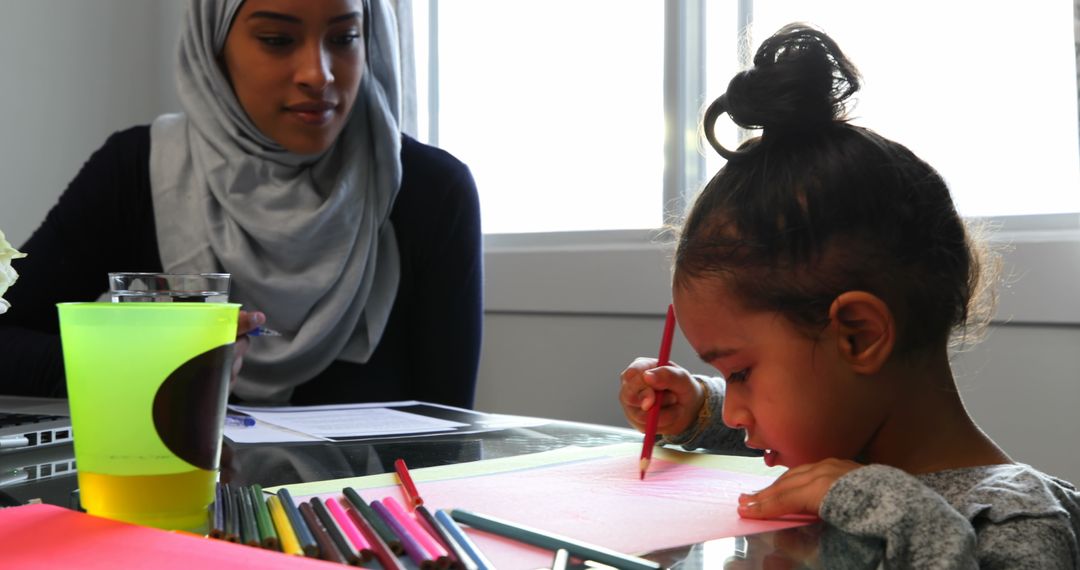 Mother in Hijab Watching Daughter Drawing at Home