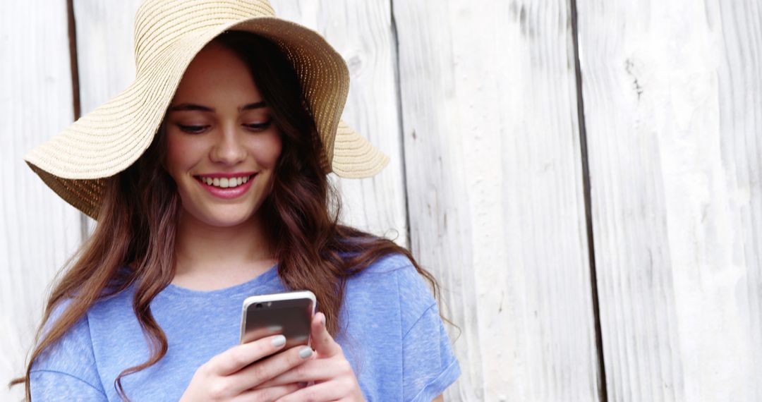 Smiling Young Woman Using Smartphone While Wearing Summer Hat - Free Images, Stock Photos and Pictures on Pikwizard.com