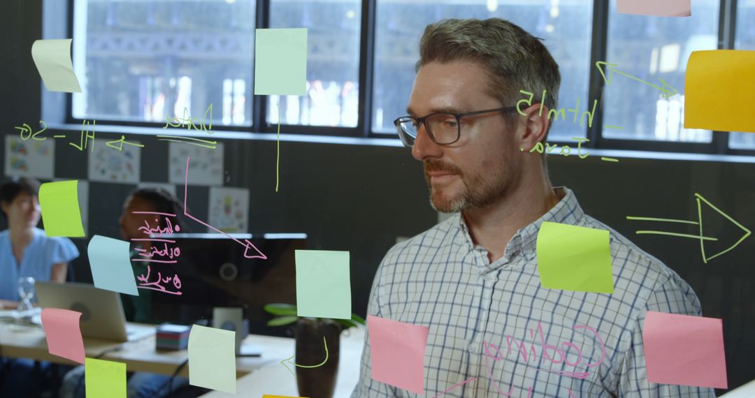 Businessman Strategizing with Sticky Notes on Glass Wall in Office - Free Images, Stock Photos and Pictures on Pikwizard.com