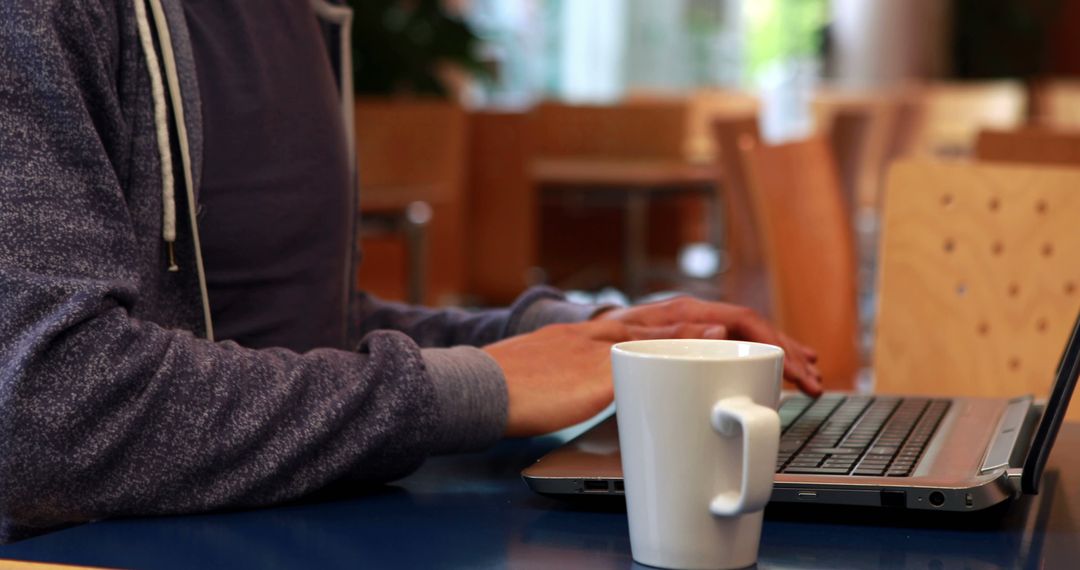 Man Typing on Laptop in Cozy Coffee Shop with White Mug in Foreground - Free Images, Stock Photos and Pictures on Pikwizard.com