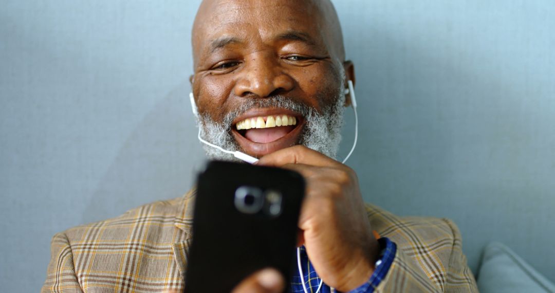 Senior African American Man Laughing while Using Smartphone with Earbuds - Free Images, Stock Photos and Pictures on Pikwizard.com