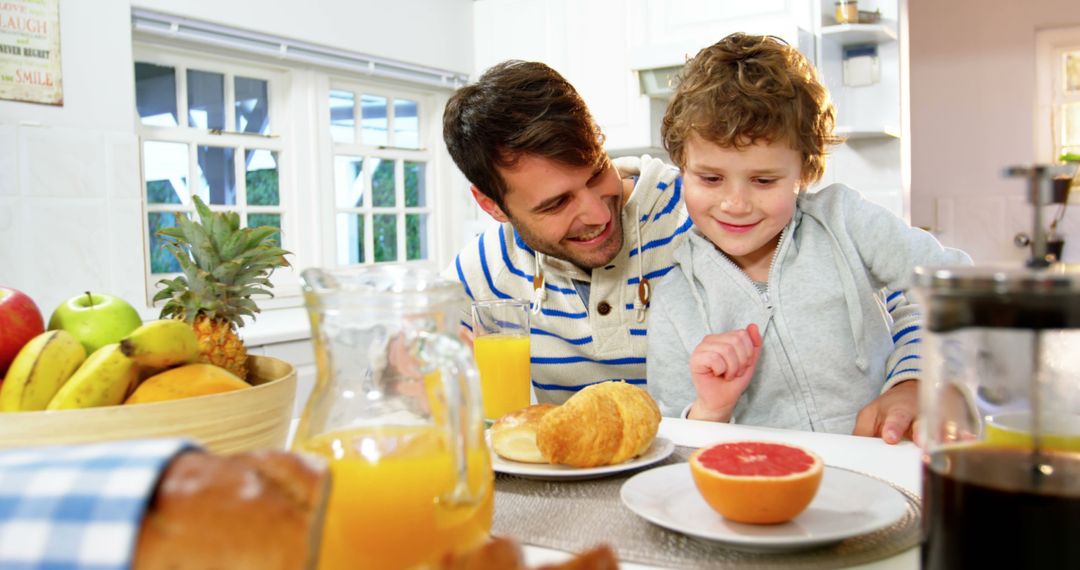 Happy father and son enjoying breakfast together in bright kitchen - Free Images, Stock Photos and Pictures on Pikwizard.com