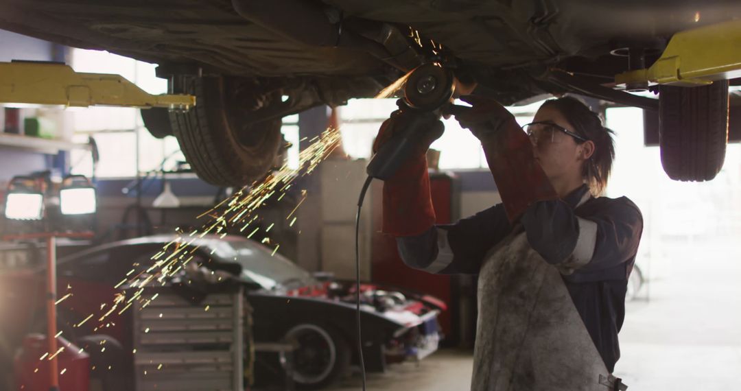 Female Mechanic Using Grinder Underneath Car in Workshop