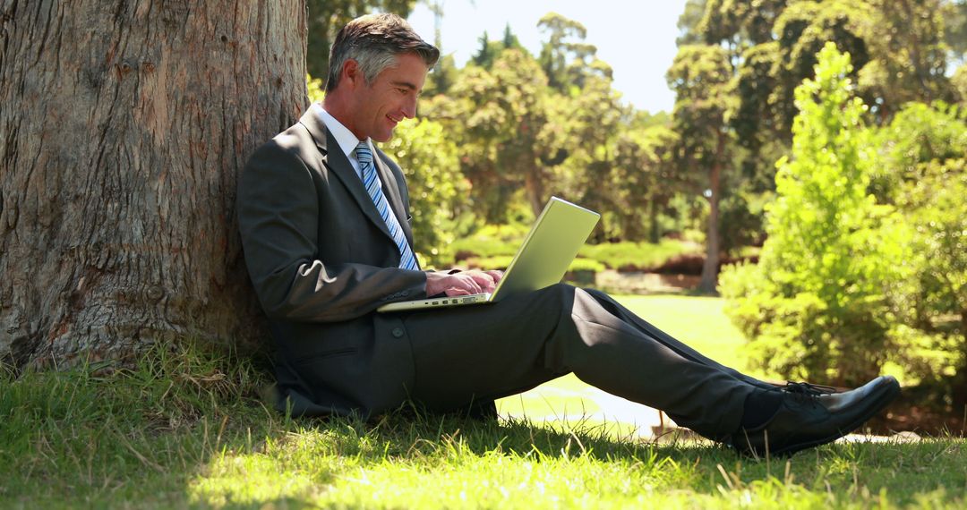 Businessman Enjoying Remote Work Under Tree in Park