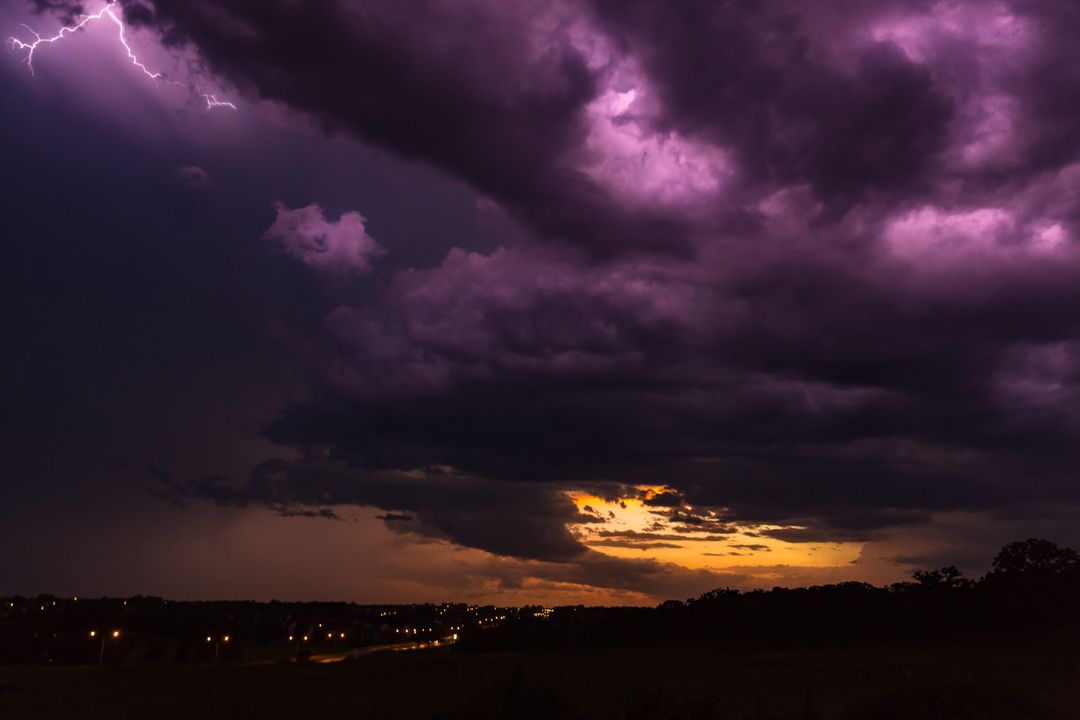 Purple thunderstorm clouds looming with lightning striking above suburban sunset lights