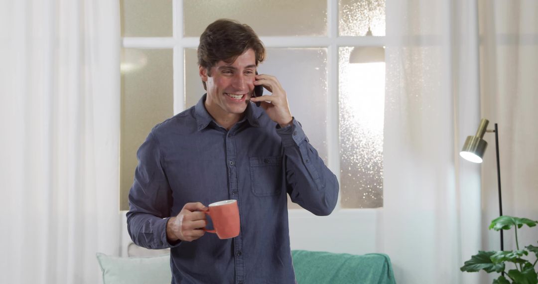 Man Smiling While Holding Mug and Phone in Relaxed Home Setting