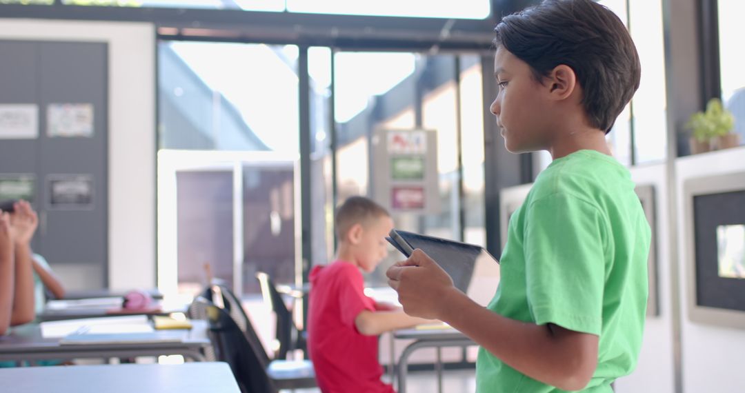 Boy in greel shirt engaged with tablet in modern classroom setting