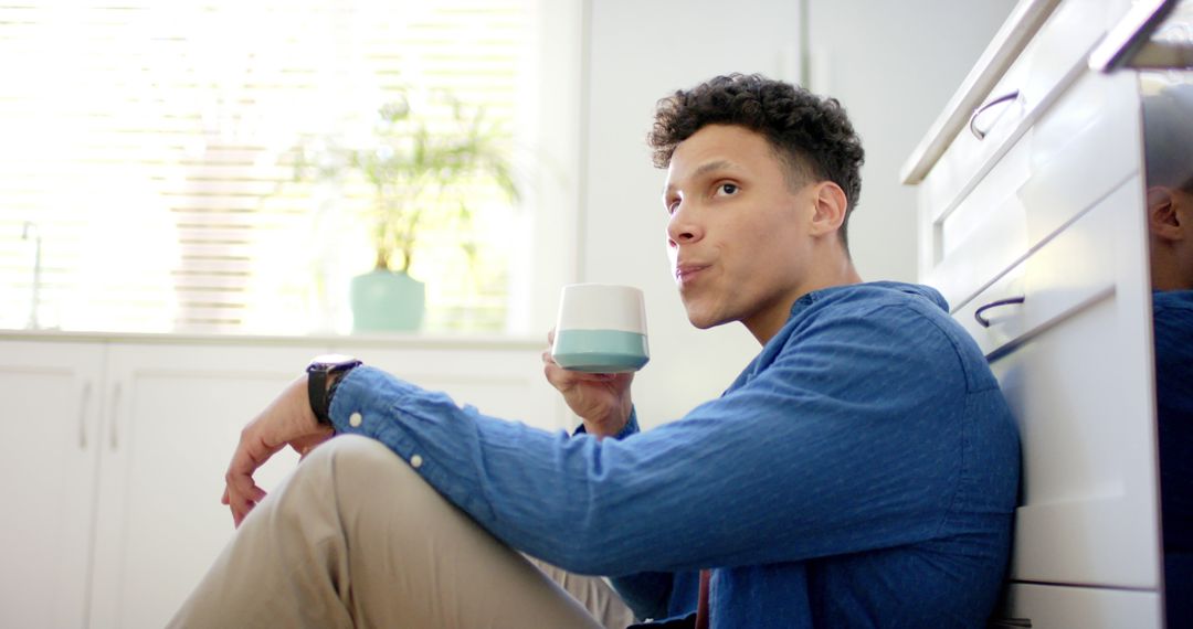 Young Man Sitting on Floor Drinking Coffee in Modern Kitchen - Free Images, Stock Photos and Pictures on Pikwizard.com