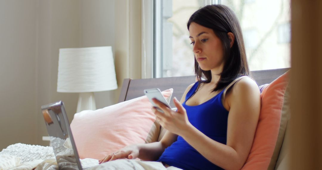 Woman Using Smartphone in Bed with Laptop Nearby - Free Images, Stock Photos and Pictures on Pikwizard.com