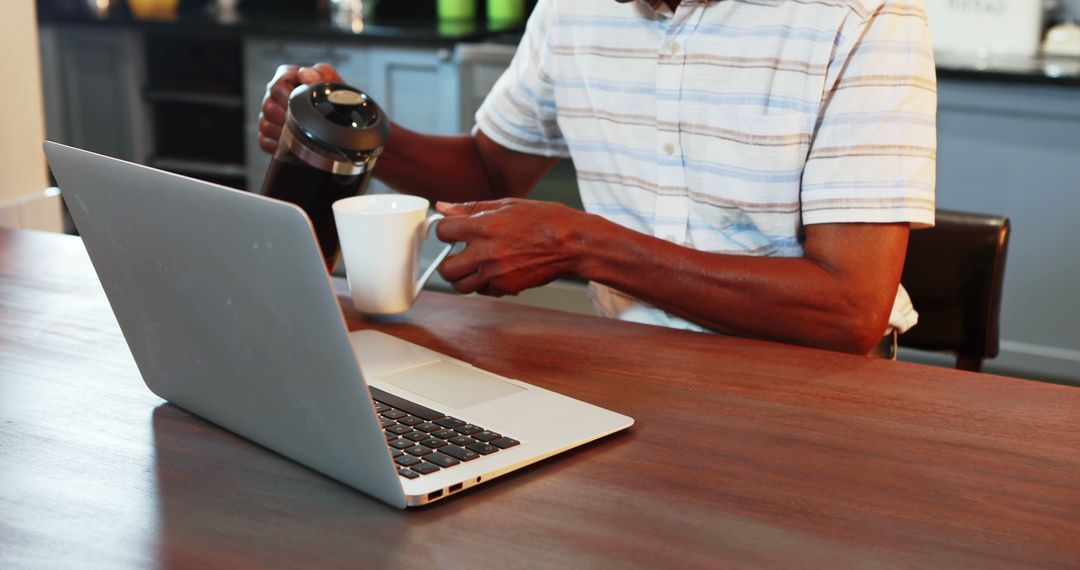 Man Pouring Coffee While Sitting at Laptop in Kitchen - Free Images, Stock Photos and Pictures on Pikwizard.com