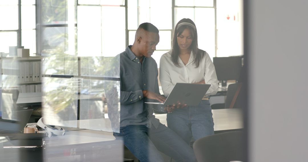 Colleagues Collaborating on Project Using Laptop in Modern Office