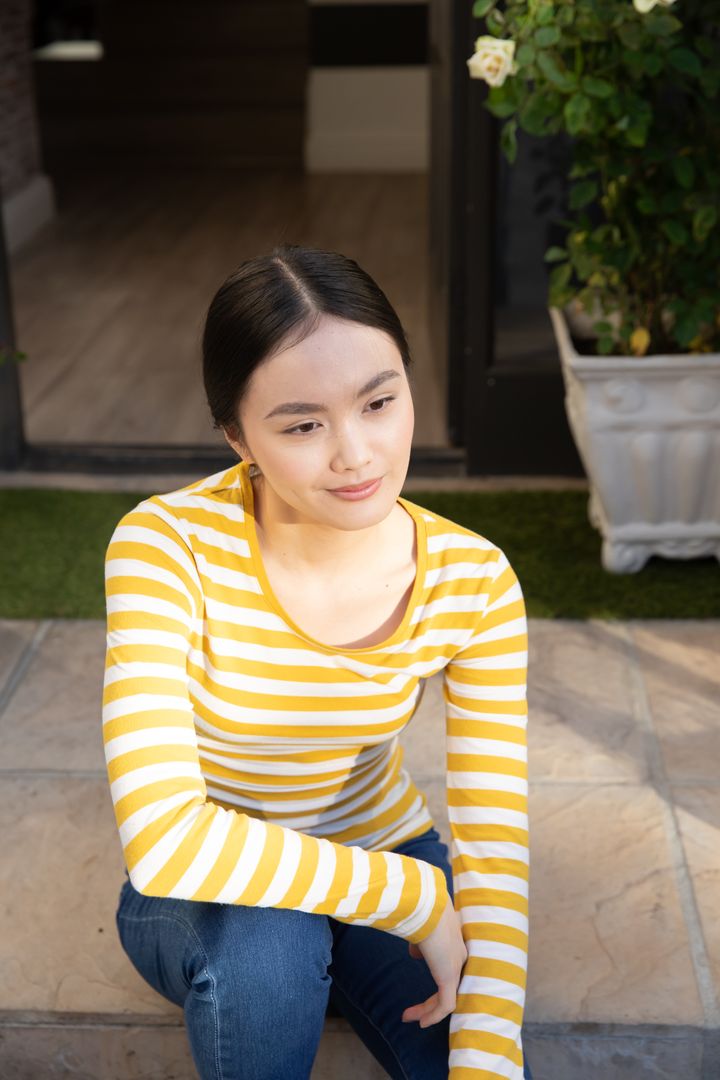 Serene Asian Woman Resting on Steps Near Greenery